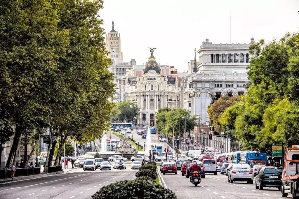 A busy urban street with historic buildings, including a prominent white building with columns and a statue on top.