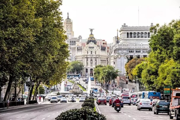 A busy urban street with historic buildings, including a prominent white building with columns and a statue on top. - LOFTS Puerta del SOL (Madrid)