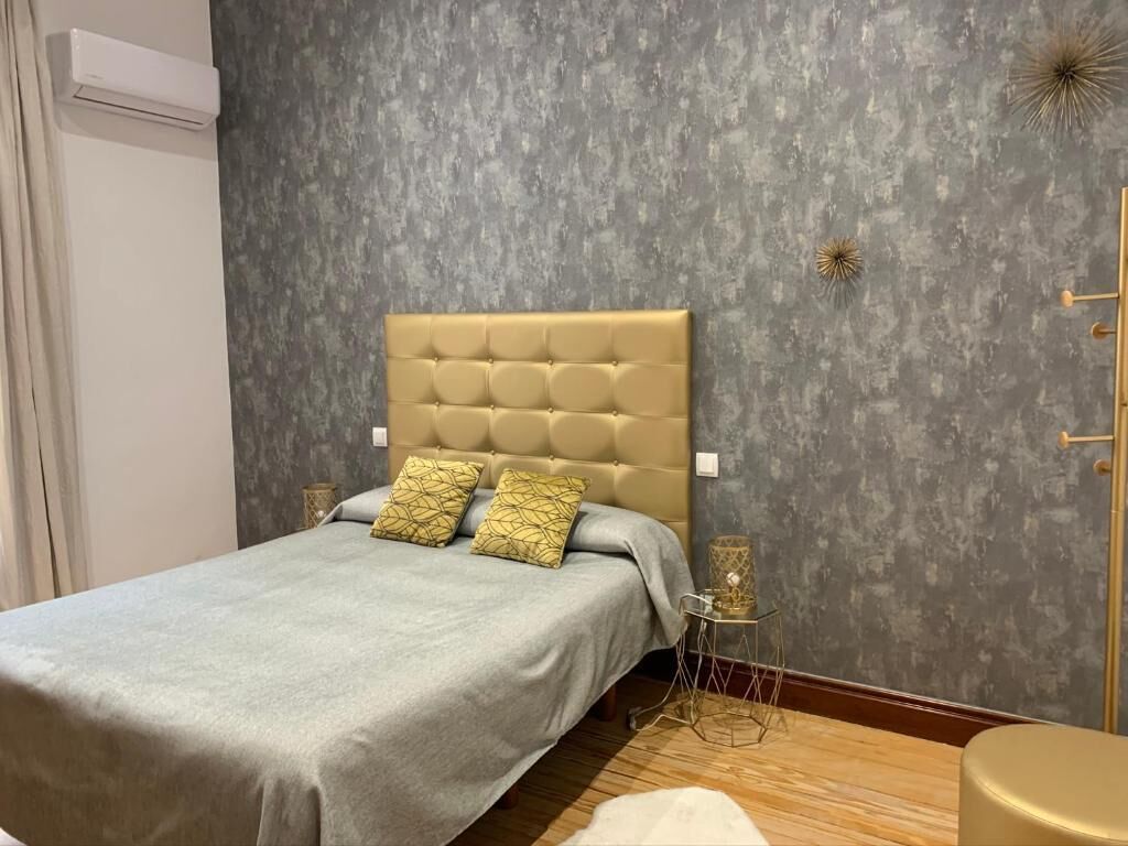 A bedroom with a tufted headboard, a grey bedspread, and two patterned pillows.