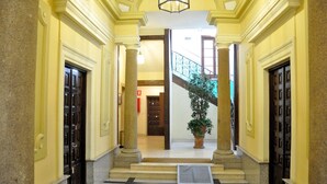 Vestíbulo de hotel con una escalera central, columnas y una planta en maceta.