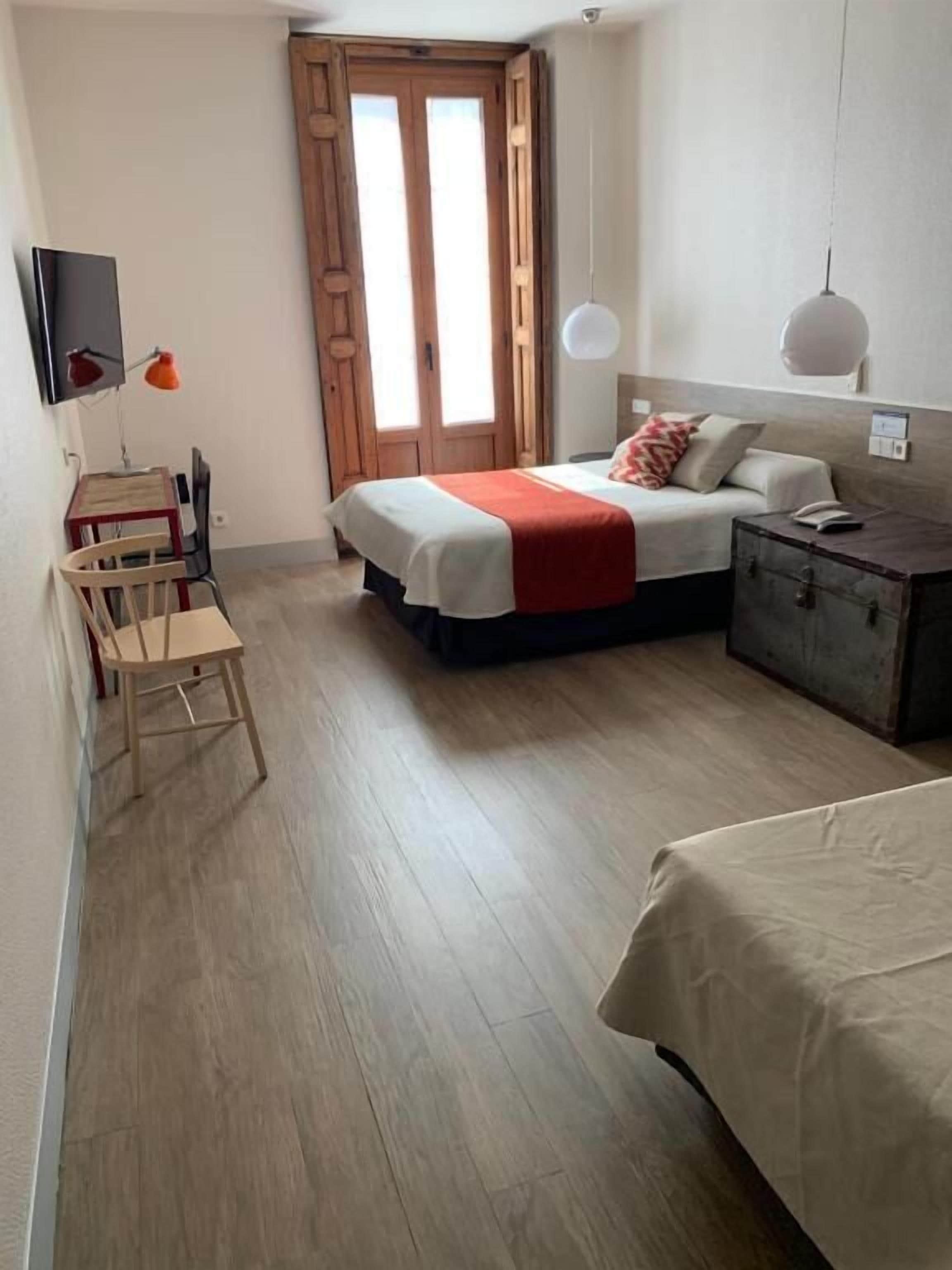 Ein Schlafzimmer mit Bett, Nachttisch, Lampe und Schreibtisch mit Stuhl.