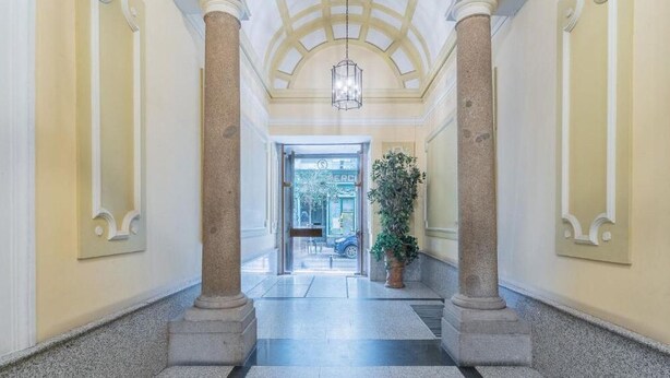 Un pasillo con columnas, una planta en maceta y una puerta que da a un espacio exterior.
