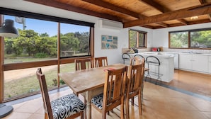 A kitchen with large windows, wooden ceiling beams, and a dining area with a table and chairs. - Aireys Rivermouth House (Aireys Inlet)