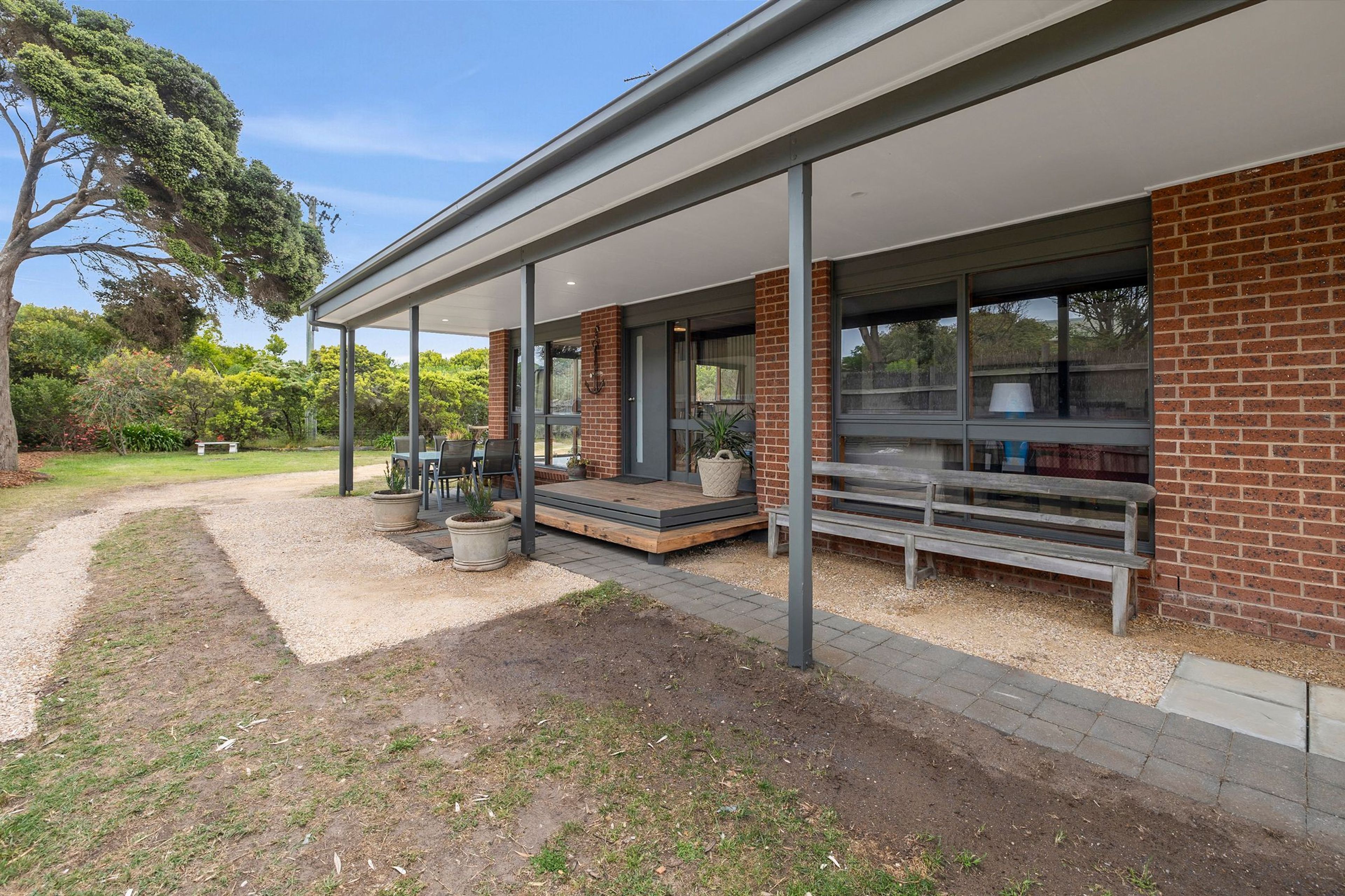 A modern building with a covered outdoor area, a brick facade, and a gravel pathway.
