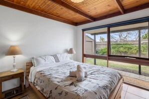 Een slaapkamer met een groot raam, een houten plafond en een bed met een beddegoed met een patroon.