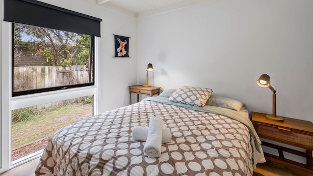 A bedroom with a large bed, two bedside tables, a window with a view, and a hanging artwork. - Aireys Rivermouth House (Aireys Inlet)