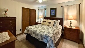 Un dormitorio con una cama, dos mesitas de noche, un aparador, un ventilador de techo y un cuadro enmarcado en la pared.