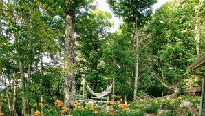 Un sendero en un jardín con una hamaca, rodeado de diversas plantas y árboles florecientes.