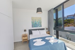 Un dormitorio moderno con una cama grande, un cuadro en la pared y vistas al exterior a través de un amplio ventanal.