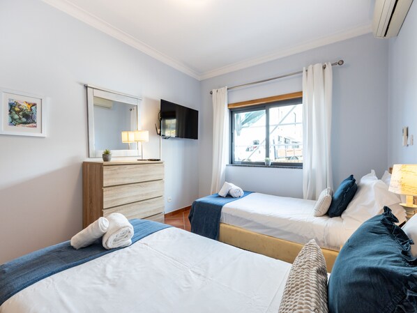 A hotel room with two beds, a TV, a dresser, a window with curtains, and a painting on the wall. - Studio Dona Ana - great studio apartment! (Lagos)