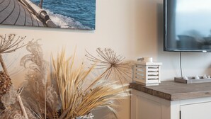 Una habitación con una televisión de pantalla plana grande montada en la pared, un mueble de madera y un arreglo decorativo de plantas.