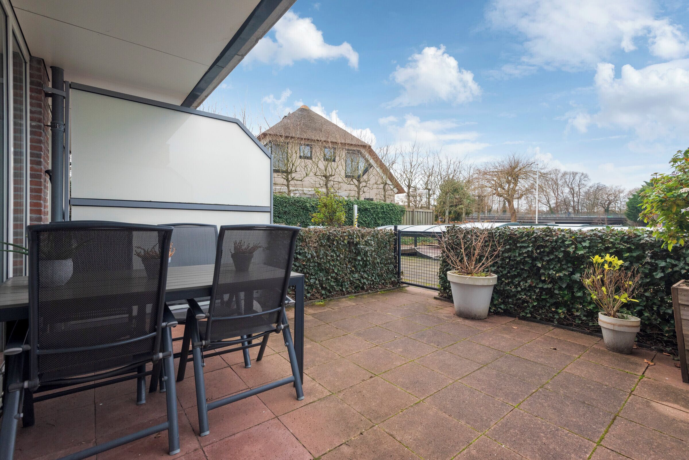 A patio with a table and chairs, a white awning, and a view of a house in the background.