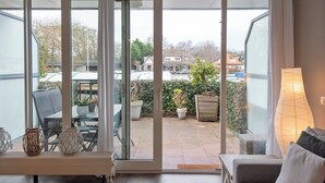 Una habitación con puerta corrediza de vidrio que da a un patio con muebles de exterior y plantas en macetas.