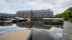 Un puerto deportivo con barcos amarrados, una terraza de madera y un edificio moderno con varios balcones al fondo.