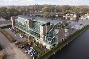 Un bâtiment moderne à la façade vitrée, avec un parking et une rivière en arrière-plan.