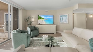 Uma sala de estar moderna com uma televisão de tela plana grande, um sofá, uma mesa de centro de vidro e um vaso com planta.
