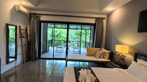 A modern hotel room with a large bed, a sofa, and a view of a garden through a glass door. - Sannot Riverside Boutique Hotel (Chiang Mai)