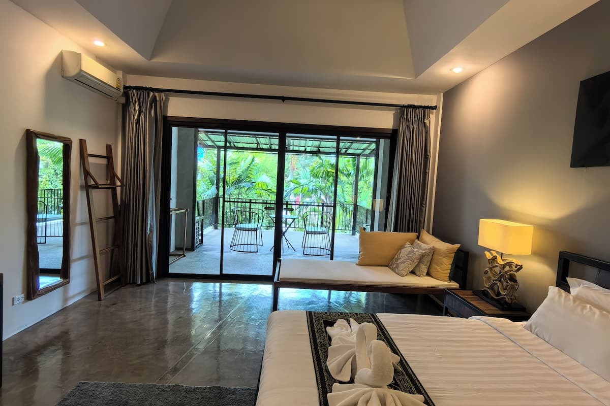A modern hotel room with a large bed, a sofa, and a view of a garden through a glass door.