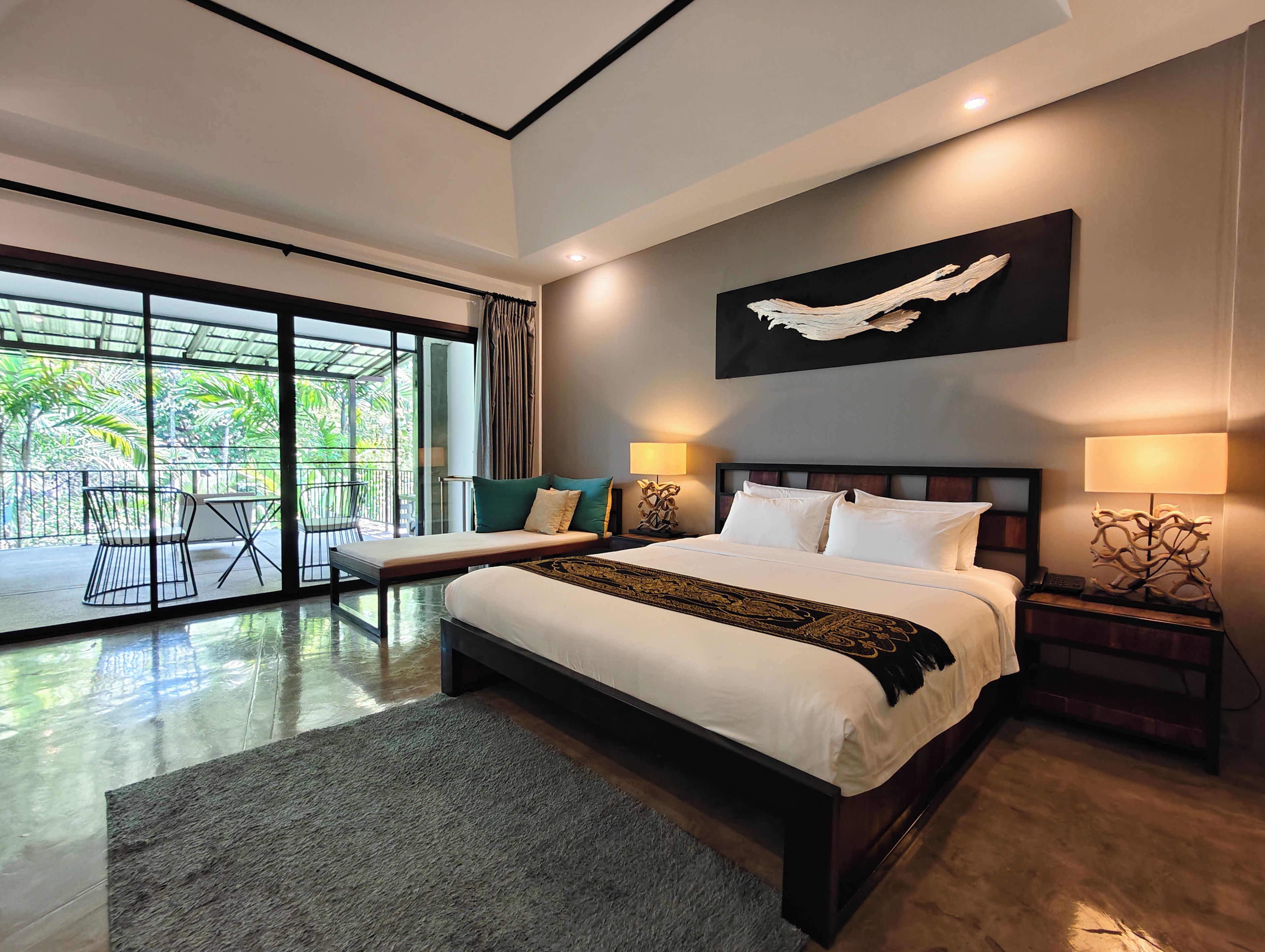 Habitación de hotel moderna con una cama grande, dos mesitas de noche, vistas a un espacio exterior mediante una puerta corrediza de vidrio y una obra de arte colgada en la pared.