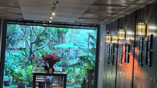 Un interior moderno con ventilador de techo, una recepción de madera y vistas a un jardín exuberante a través de amplios ventanales.