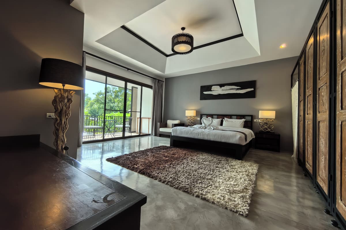 A modern bedroom with a large bed, a desk, and a view of the outdoors.
