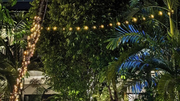 A nighttime garden with a water feature, string lights, and lush greenery. - Sannot Riverside Boutique Hotel (Chiang Mai)
