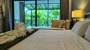 A hotel room with a bed, a sofa, a window with a view of greenery, and a lamp. - Sannot Riverside Boutique Hotel (Chiang Mai)