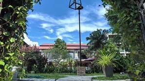 Un jardín con un sendero, un farol colgante y un edificio de techo rojo al fondo.