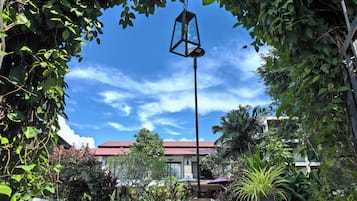 A garden with a pathway, a hanging lantern, and a building with a red roof in the background.