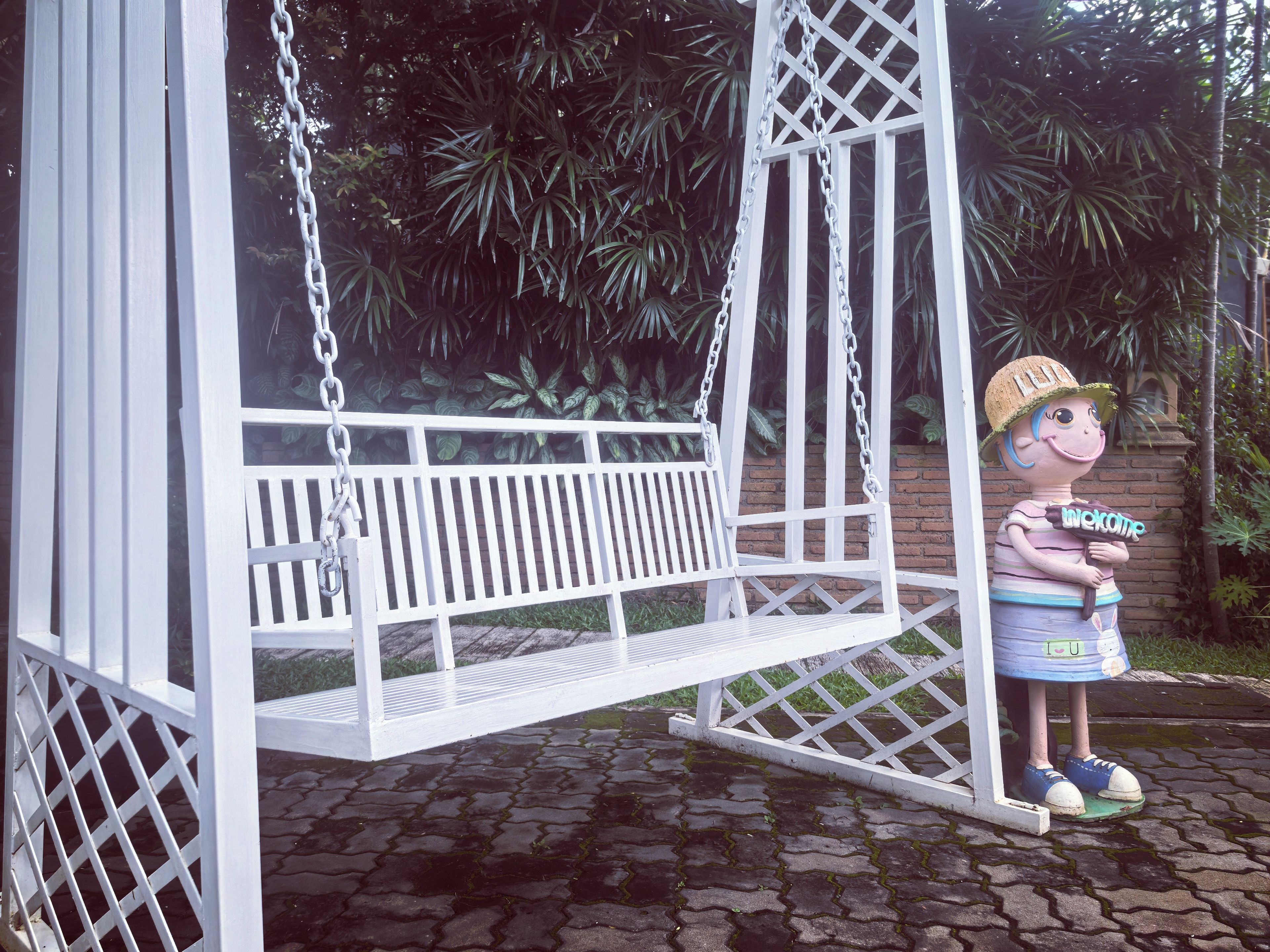 A white swing set with a bench, surrounded by greenery.