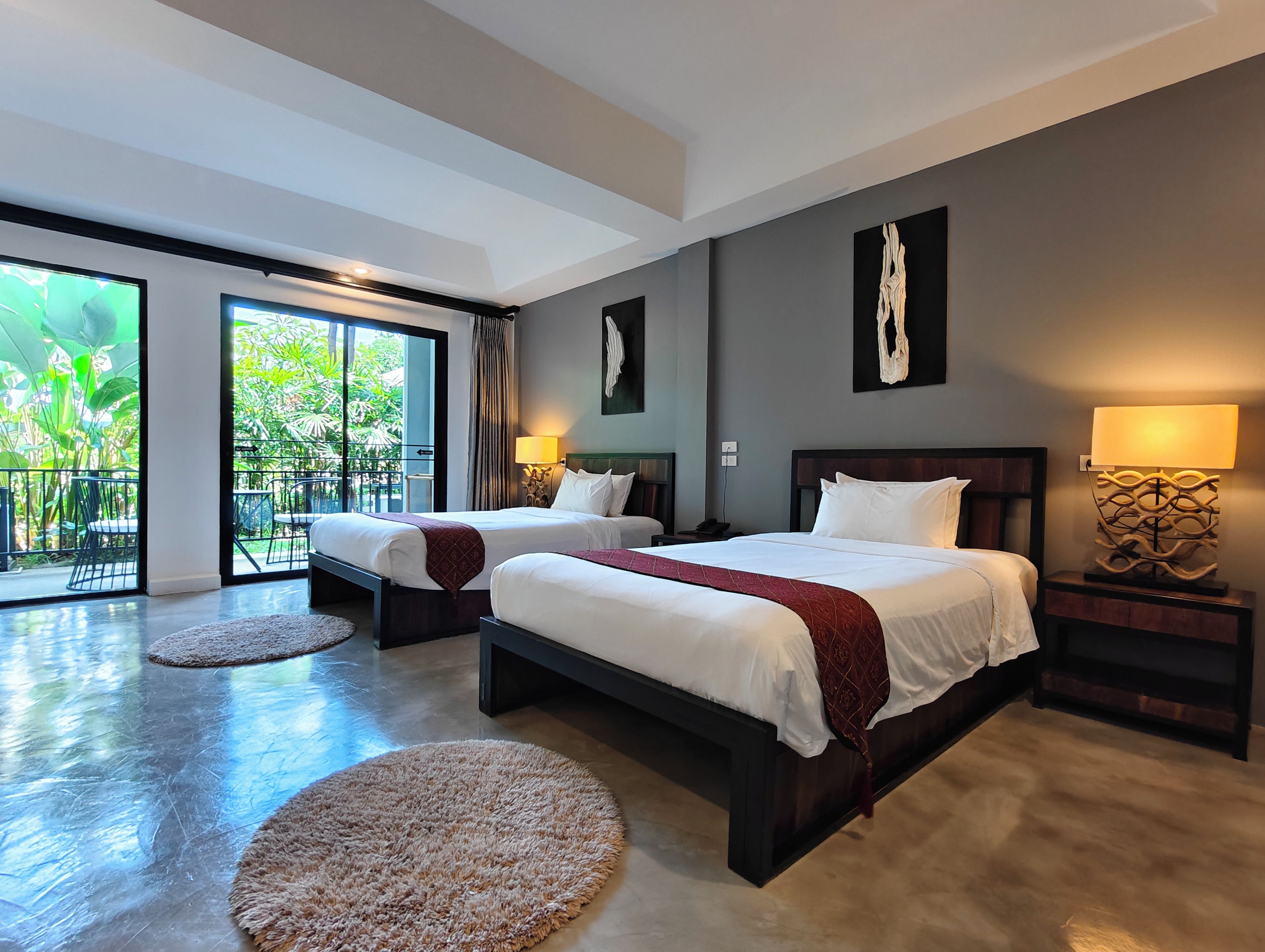 A hotel room with two beds, a balcony with a view of greenery, and a modern design.