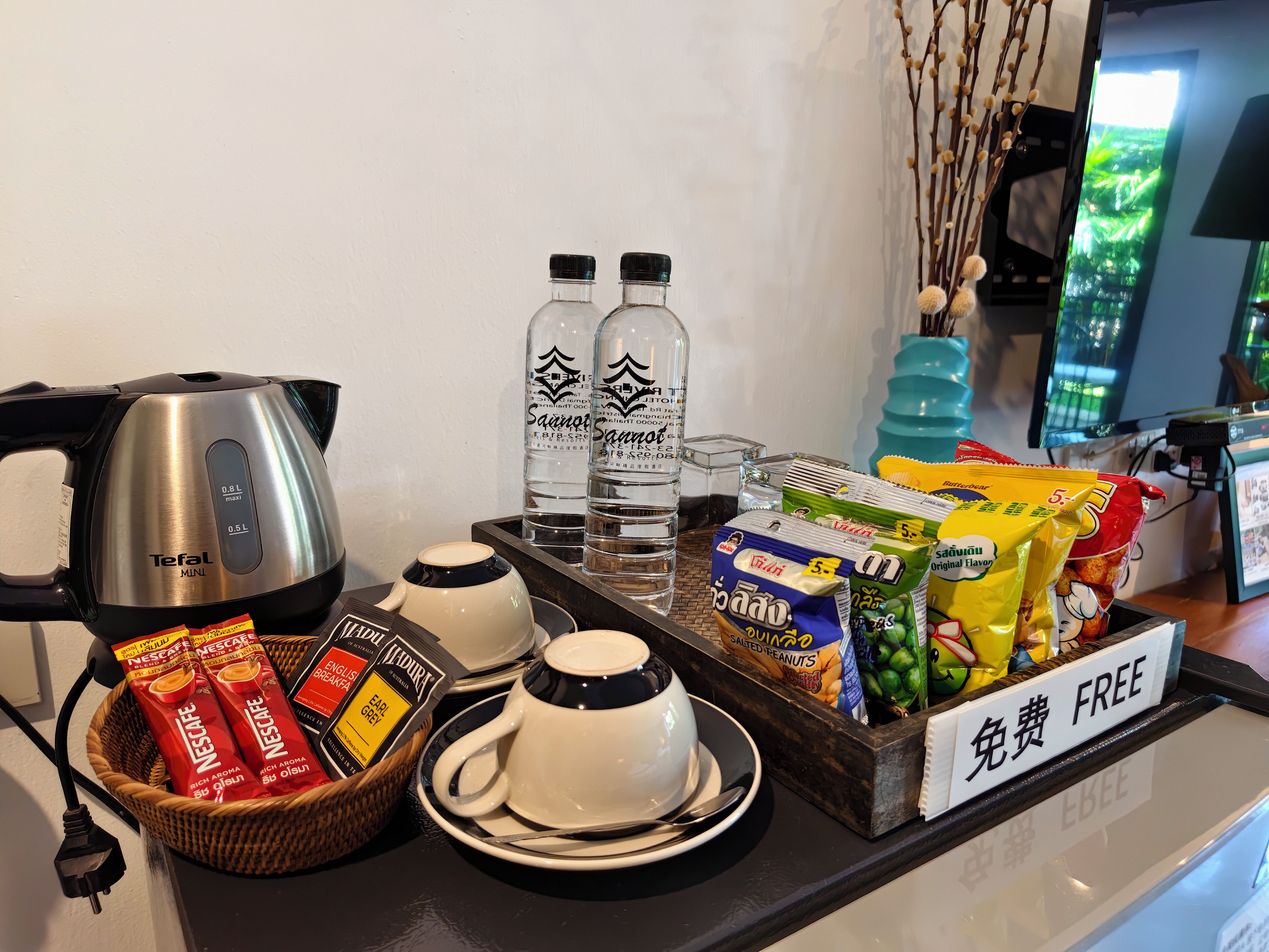 A breakfast setup with a coffee maker, water bottles, a basket of Nescafe, and snacks.