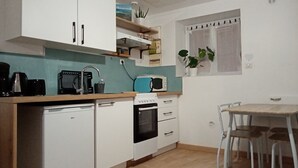 Ett kompakt kök med vita skåp, en mikrovågsugn, en brödrost och ett handfat. Det finns en liten matplats med ett bord och stolar.