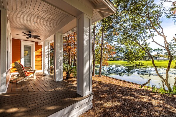 A covered porch with a ceiling fan, a chair, and a view of a pond and trees.