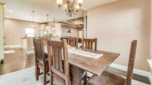 Een eetruimte met een houten tafel en stoelen, een kroonluchter en een keuken op de achtergrond.