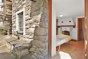 A stone-walled room with a bed, a window with bars, and a small table with a plant. - Rustico Esterina (Sonogno)