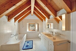 A modern bathroom with a bathtub, a large mirror, and a window. - Rustico Esterina (Sonogno)