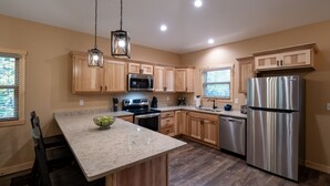 A modern kitchen with wooden cabinets, stainless steel appliances, and a marble countertop. - New! 4BR Lake Namakagon Cabin - Sleeps 15 - Lakefront w/ boat access (Cable)