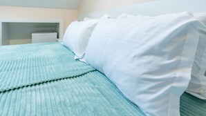 Una cama bien hecha con una colcha azul texturizada y almohadas blancas.