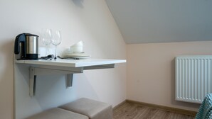 Una pequeña kitchenette con un hervidor, dos copas de vino y una taza sobre un estante blanco.