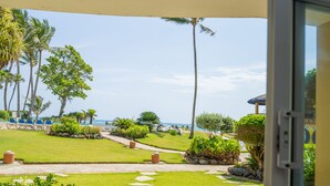 Eine Terrasse mit Blick auf einen Strand, Palmen und eine Rasenfläche mit einem Weg.