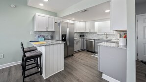 A modern kitchen with white cabinets, a stainless steel refrigerator, a built-in oven, and a granite countertop.