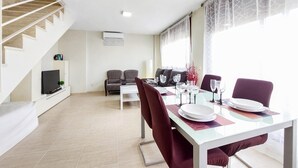 Un comedor con una mesa de vidrio, sillas rojas y un televisor sobre un mueble blanco.