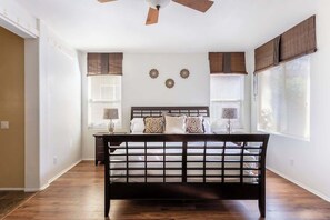 Un dormitorio con cama de madera, dos mesitas de noche, un ventilador de techo y tres apliques de pared.