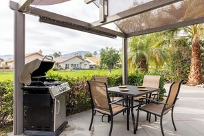 Un patio al aire libre con una parrilla, una mesa y sillas.