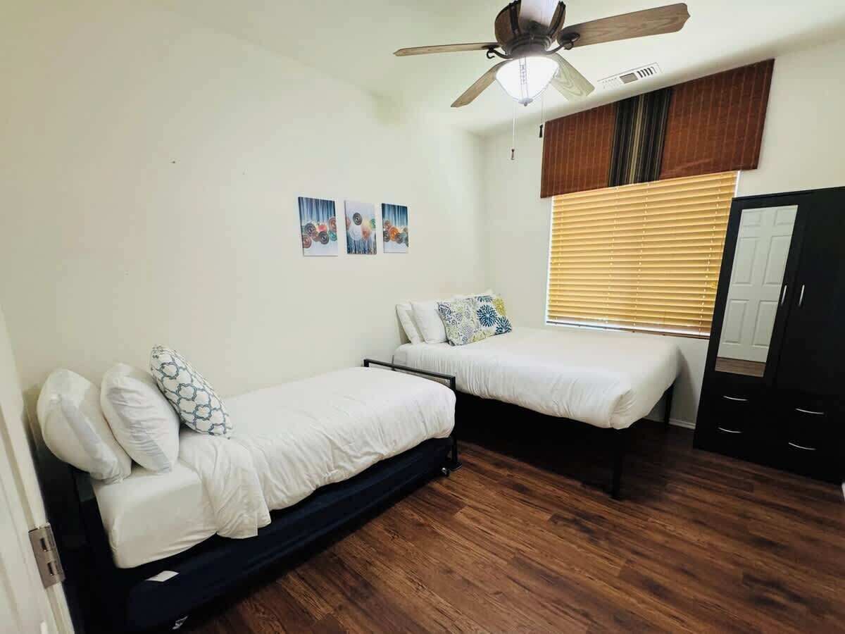 Un dormitorio con dos camas, ventilador de techo, suelo de madera y armario.