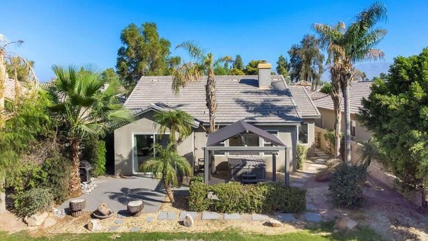 A modern house with a covered patio, surrounded by palm trees and a well-maintained garden. - Cozy Home in Gated Country Club (Indio)