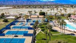 A resort with multiple tennis courts, a swimming pool, and palm trees. - Cozy Home in Gated Country Club (Indio)