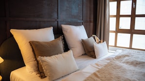 A bed with multiple pillows and a blanket, a wooden headboard, and a window with curtains. - The Charming by Curt Suites (Berlin)