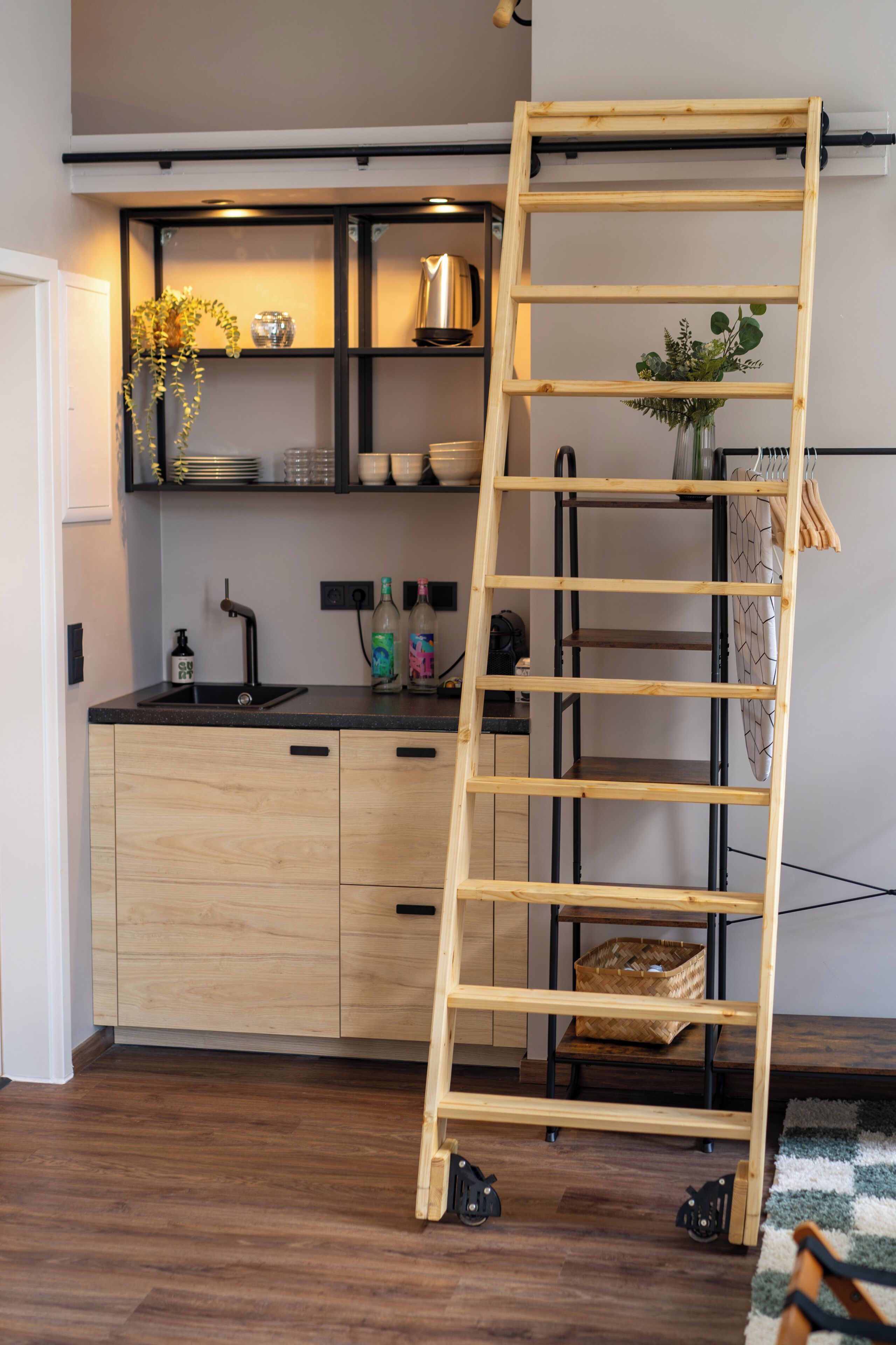 Cucina con pensili in legno, lavello nero e una scala in legno appoggiata al muro.